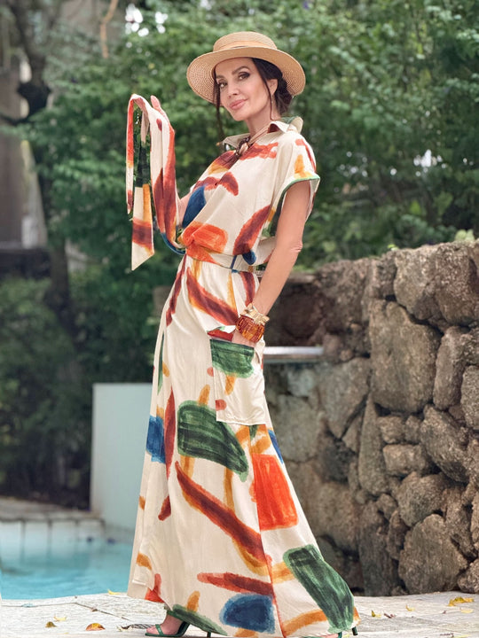 Mulher usando conjunto de saia longa estampada com traços coloridos e chapéu de palha ao ar livre