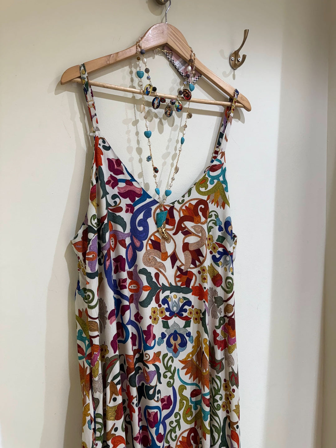 Vestido de alças estampado com padrão colorido floral e colar de pedras pendurado em cabide.