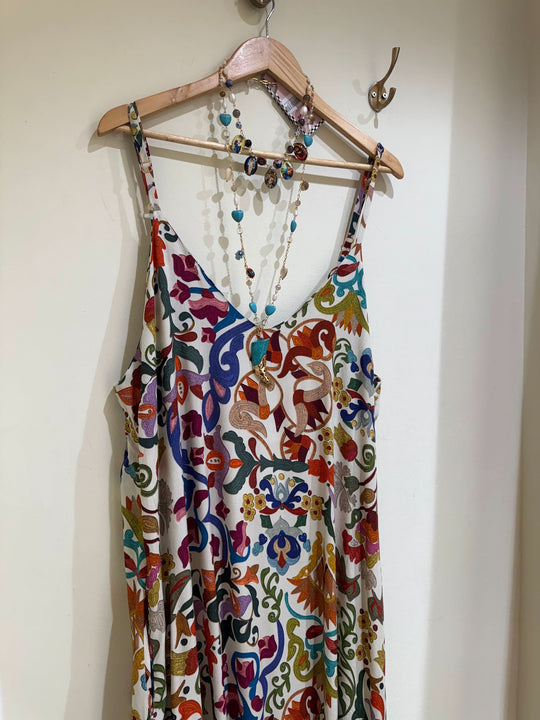 Vestido de alças estampado com padrão colorido floral e colar de pedras pendurado em cabide.