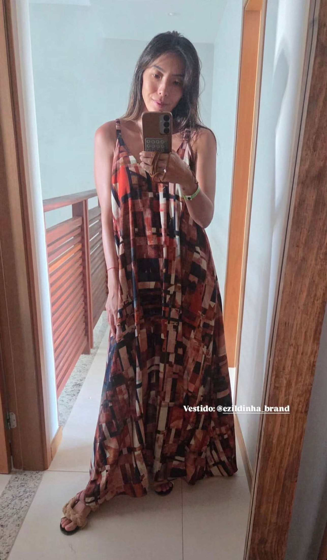 Mulher usando vestido longo de alça com estampa geométrica colorida em frente ao espelho