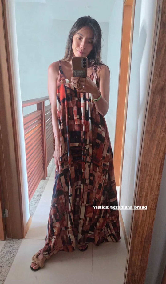 Mulher usando vestido longo de alça com estampa geométrica colorida em frente ao espelho