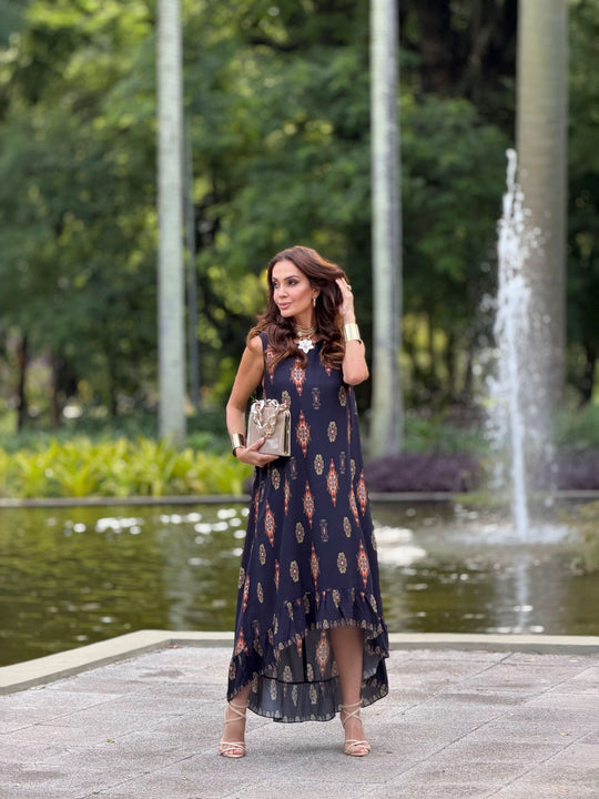 Mulher usando vestido longo de viscose estampado em ambiente externo com fonte e vegetação ao fundo.