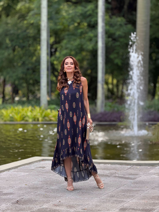 Mulher usando vestido longo de viscose estampado, elegante, ao ar livre em frente a fonte.