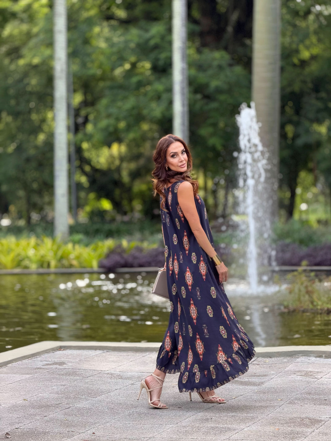 Mulher usando vestido longo estampado de viscose, ao ar livre perto de fonte e natureza.