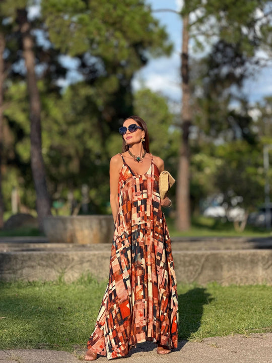Mulher usando vestido longo de alças com estampa geométrica colorida em ambiente ao ar livre