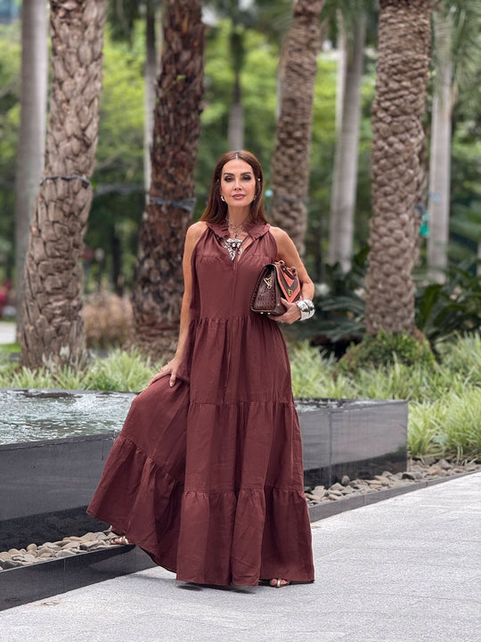 Mulher usando vestido longo de linho puro marrom, ao ar livre perto de palmeiras.